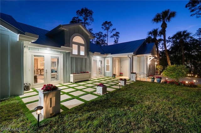 back house at dusk featuring french doors and a lawn