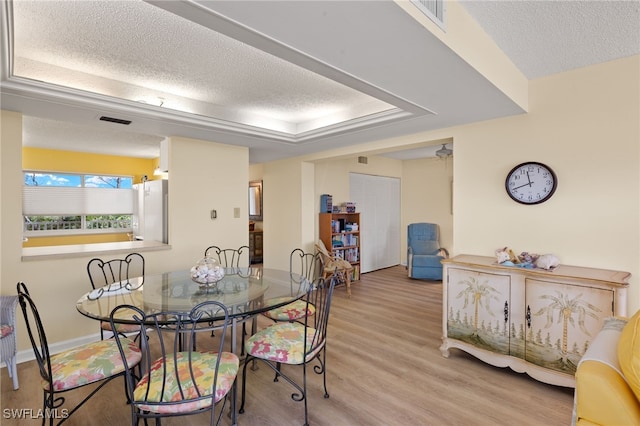 dining area featuring light wood-type flooring, a tray ceiling, visible vents, and a textured ceiling