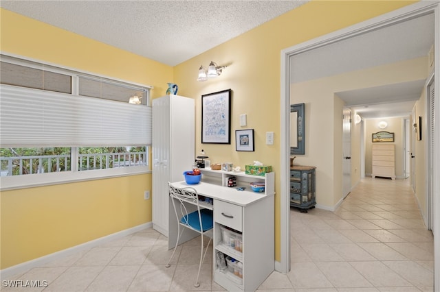 office area with a textured ceiling, light tile patterned flooring, and baseboards