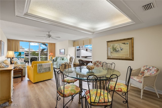 dining space featuring a textured ceiling, a ceiling fan, visible vents, baseboards, and light wood finished floors