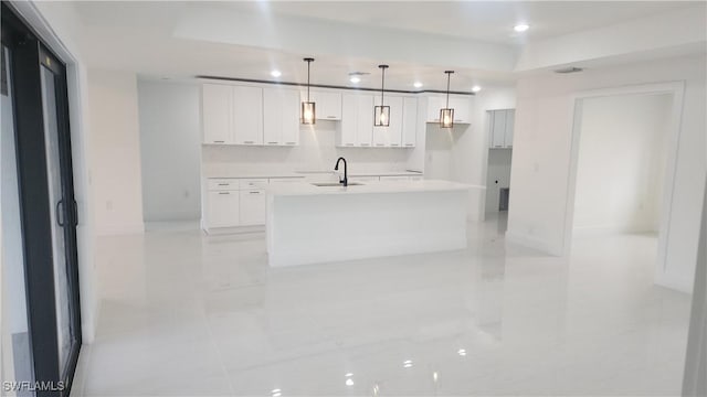 kitchen featuring white cabinetry, sink, hanging light fixtures, backsplash, and a kitchen island with sink