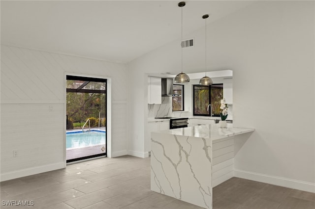 kitchen with wall chimney exhaust hood, decorative light fixtures, white cabinetry, kitchen peninsula, and light stone counters