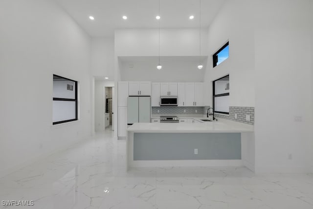 kitchen with kitchen peninsula, hanging light fixtures, white cabinetry, a towering ceiling, and white appliances