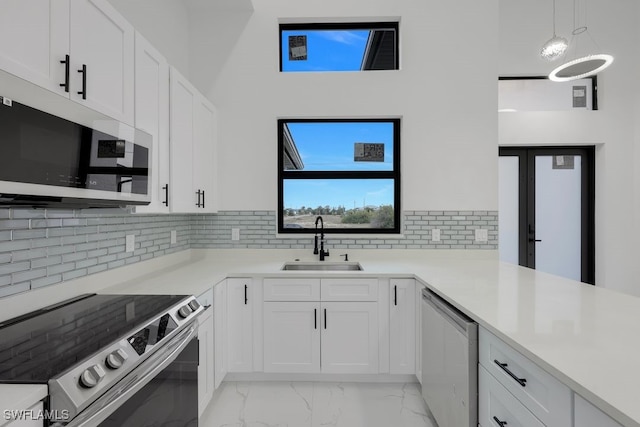 kitchen featuring tasteful backsplash, sink, white cabinets, decorative light fixtures, and stainless steel appliances