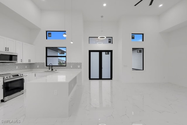 kitchen with a high ceiling, pendant lighting, white cabinets, and stainless steel range with electric cooktop