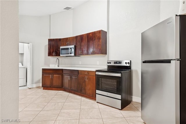 kitchen featuring sink, light tile patterned floors, appliances with stainless steel finishes, a towering ceiling, and washer / clothes dryer