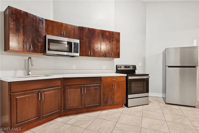 kitchen featuring dark brown cabinetry, sink, light tile patterned floors, and stainless steel appliances