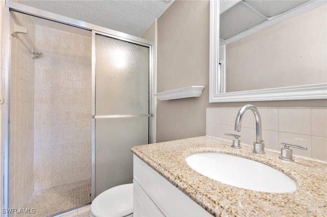 bathroom featuring vanity, a textured ceiling, decorative backsplash, a shower with shower door, and toilet