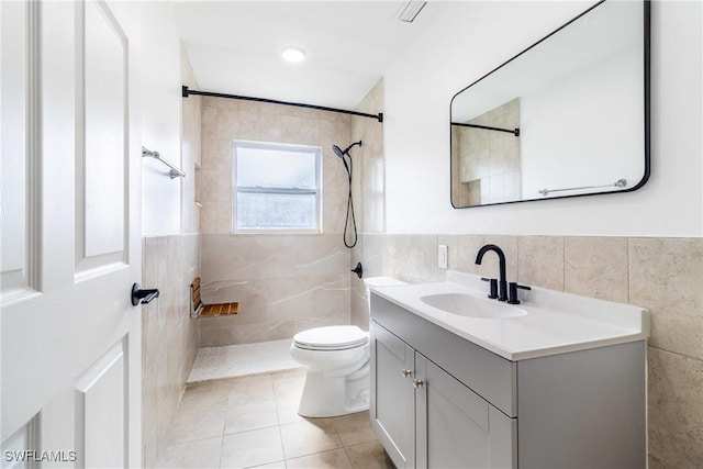 bathroom with tile walls, vanity, tiled shower, toilet, and tile patterned floors