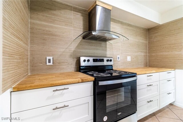 kitchen featuring electric stove, wooden counters, light tile patterned floors, white cabinets, and wall chimney exhaust hood