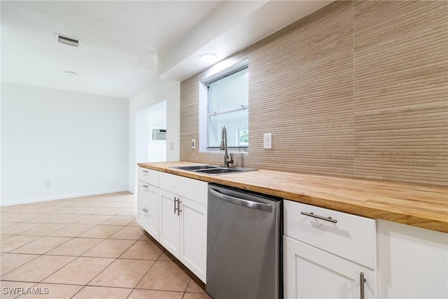 kitchen with light tile patterned floors, wooden counters, dishwasher, white cabinets, and sink