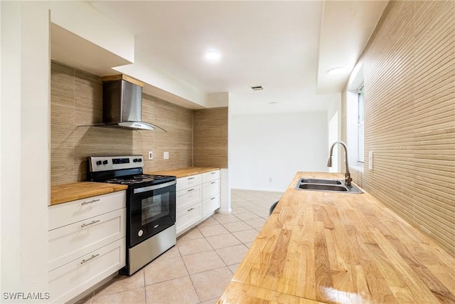 kitchen with stainless steel electric range oven, butcher block countertops, white cabinetry, sink, and wall chimney exhaust hood