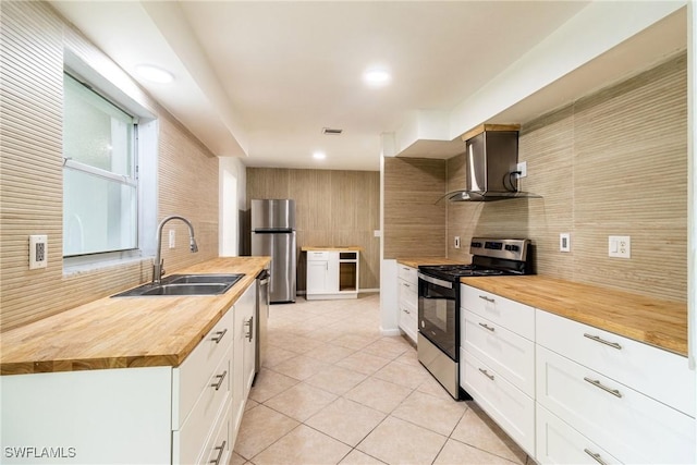 kitchen with white cabinetry, butcher block countertops, appliances with stainless steel finishes, wall chimney exhaust hood, and sink