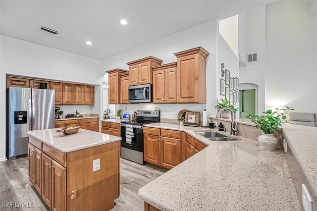 kitchen with light stone countertops, sink, appliances with stainless steel finishes, and a center island