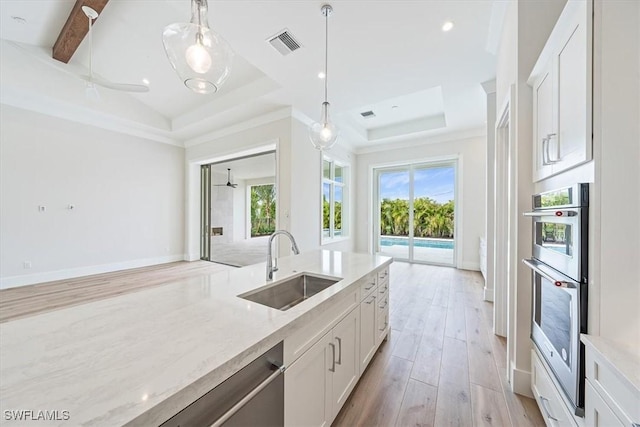 kitchen featuring white cabinetry, pendant lighting, a tray ceiling, and sink