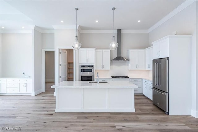 kitchen with wall chimney range hood, a center island with sink, white cabinetry, hanging light fixtures, and appliances with stainless steel finishes