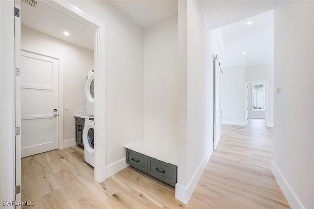 hall with stacked washer / drying machine, a barn door, and light hardwood / wood-style flooring