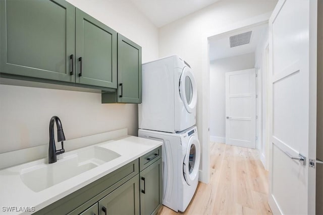 washroom with stacked washer and dryer, cabinets, light wood-type flooring, and sink