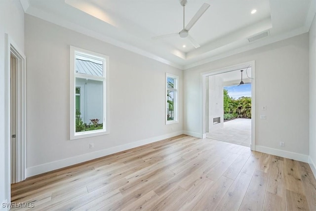 empty room featuring a raised ceiling, ceiling fan, ornamental molding, and light hardwood / wood-style flooring