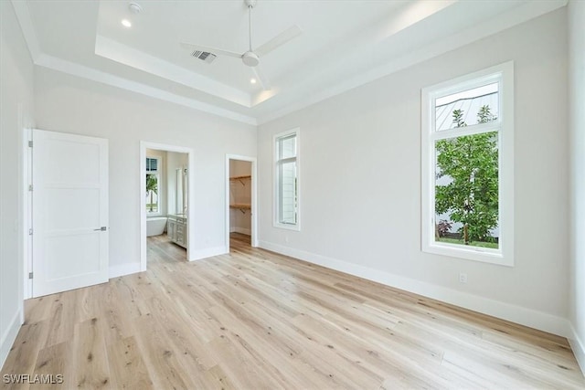 unfurnished bedroom featuring a tray ceiling, light wood-type flooring, a spacious closet, connected bathroom, and a closet