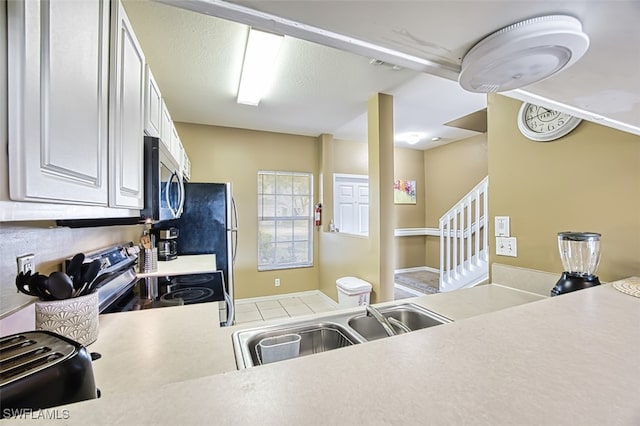 kitchen with a textured ceiling, a sink, white cabinets, light countertops, and appliances with stainless steel finishes