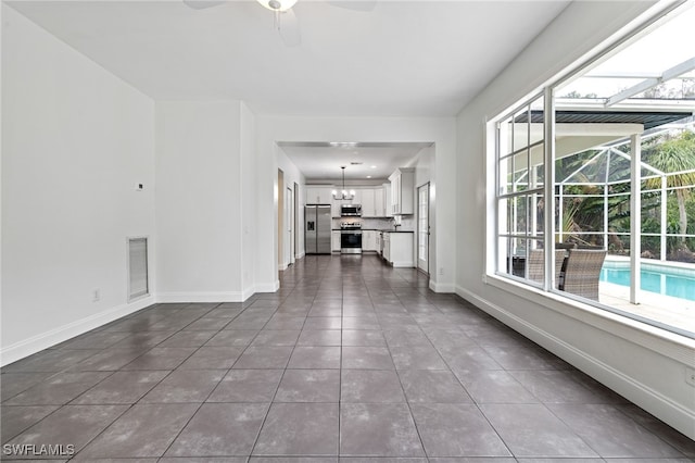 unfurnished living room featuring ceiling fan with notable chandelier and dark tile patterned floors