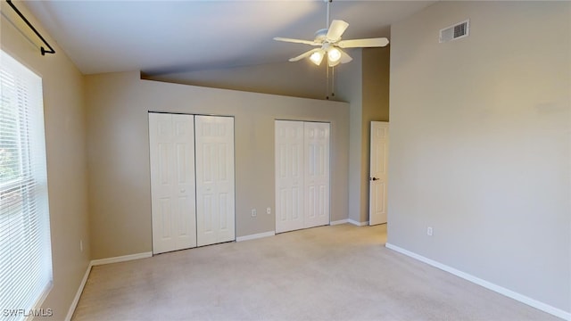 unfurnished bedroom featuring multiple closets, ceiling fan, lofted ceiling, and light colored carpet