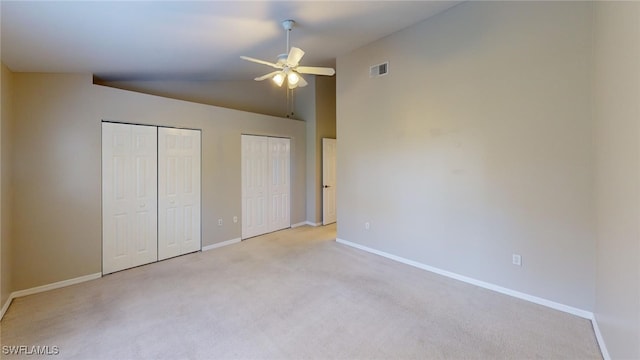 unfurnished bedroom featuring lofted ceiling, two closets, light colored carpet, and ceiling fan