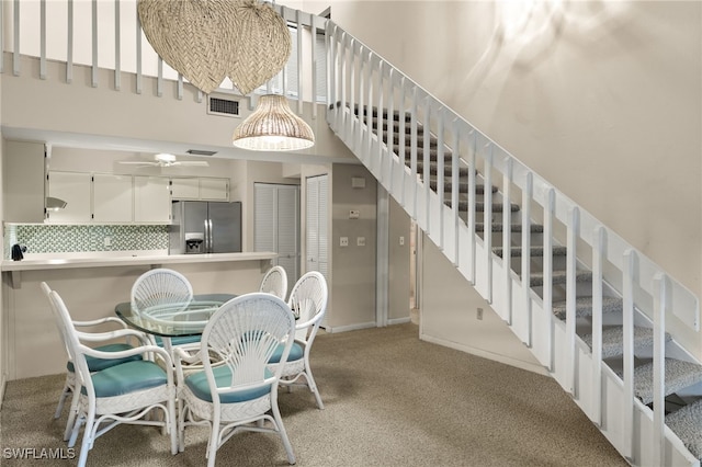 carpeted dining space featuring ceiling fan and a towering ceiling