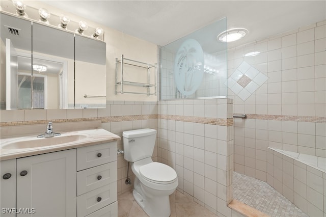 bathroom featuring toilet, tile walls, tiled shower, tile patterned floors, and vanity