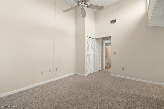 unfurnished room with a high ceiling, ceiling fan, and carpet flooring