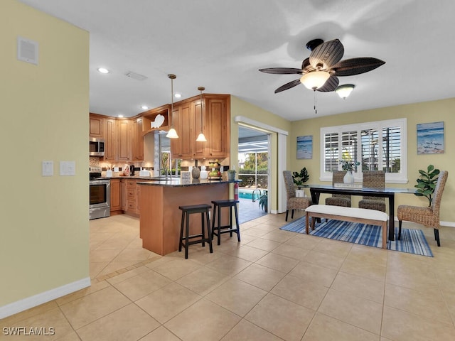 kitchen with appliances with stainless steel finishes, decorative light fixtures, a breakfast bar, ceiling fan, and light tile patterned flooring