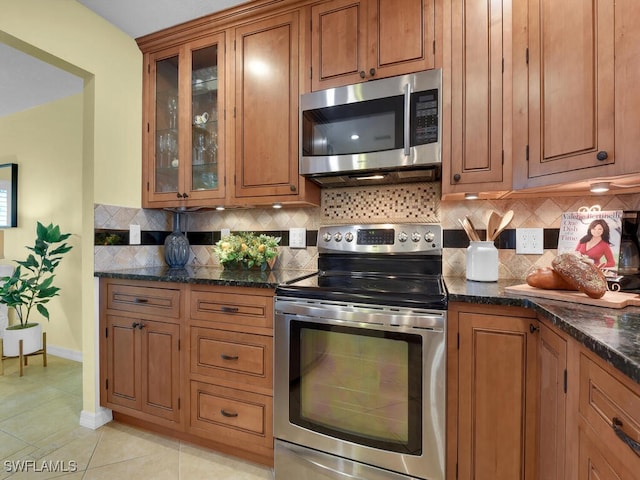 kitchen featuring stainless steel appliances, dark stone countertops, light tile patterned floors, and backsplash