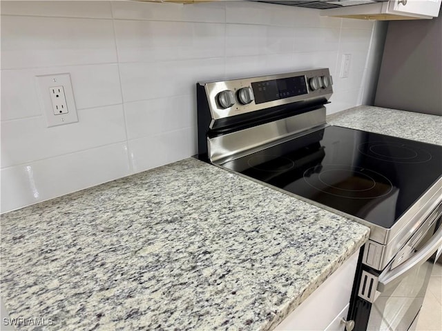 kitchen featuring white cabinets, backsplash, light stone counters, and stainless steel electric range