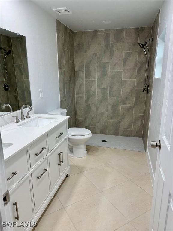 bathroom featuring tiled shower, toilet, tile patterned floors, and vanity