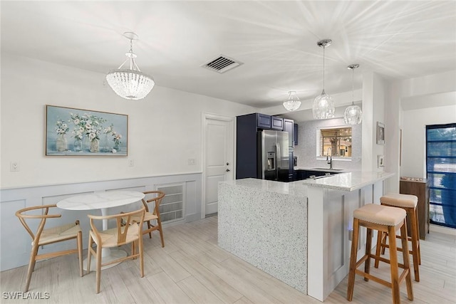 kitchen with decorative light fixtures, blue cabinetry, stainless steel fridge with ice dispenser, kitchen peninsula, and a breakfast bar area