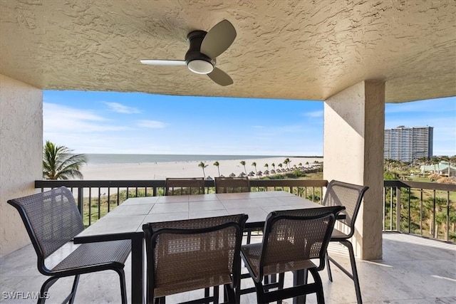 view of patio featuring a water view, ceiling fan, a balcony, and a beach view