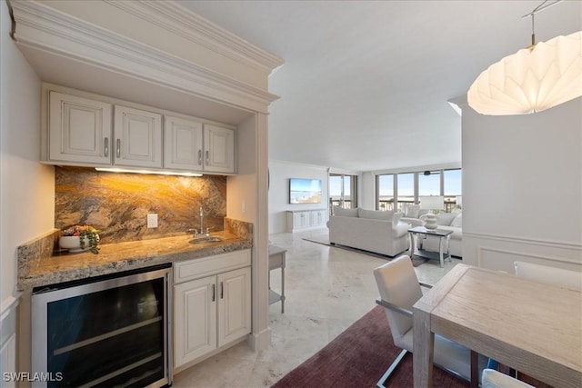 kitchen with white cabinetry, tasteful backsplash, beverage cooler, ornamental molding, and light stone counters