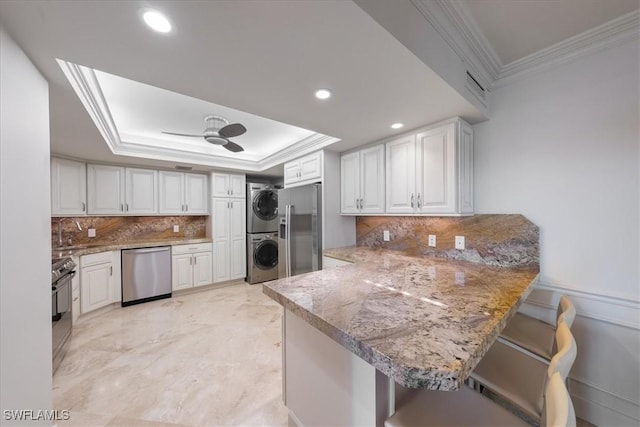 kitchen featuring a breakfast bar, kitchen peninsula, white cabinetry, stacked washer and dryer, and appliances with stainless steel finishes