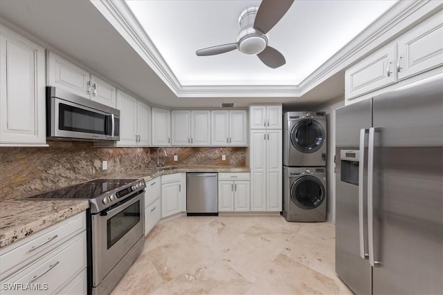 kitchen with stacked washing maching and dryer, stainless steel appliances, and white cabinetry