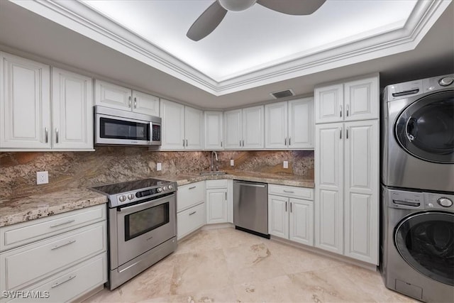 kitchen featuring white cabinets, appliances with stainless steel finishes, crown molding, and stacked washer and dryer