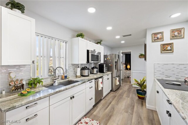 kitchen with light stone counters, sink, white cabinets, and appliances with stainless steel finishes