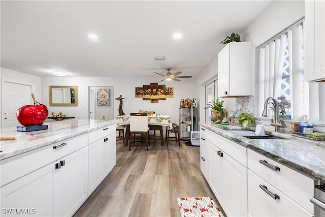 kitchen with ceiling fan, light wood-type flooring, white cabinets, light stone counters, and sink