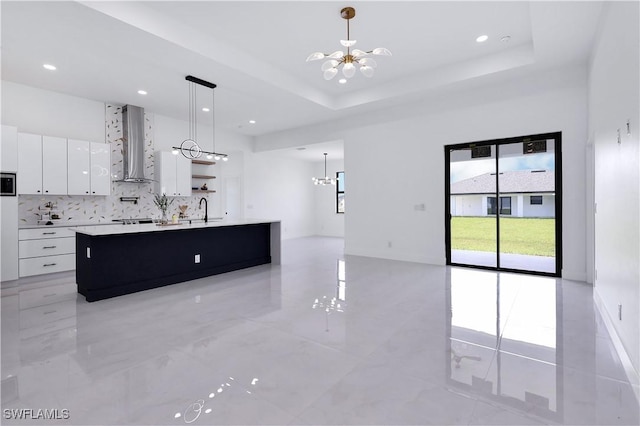 kitchen with an inviting chandelier, white cabinetry, a raised ceiling, and an island with sink