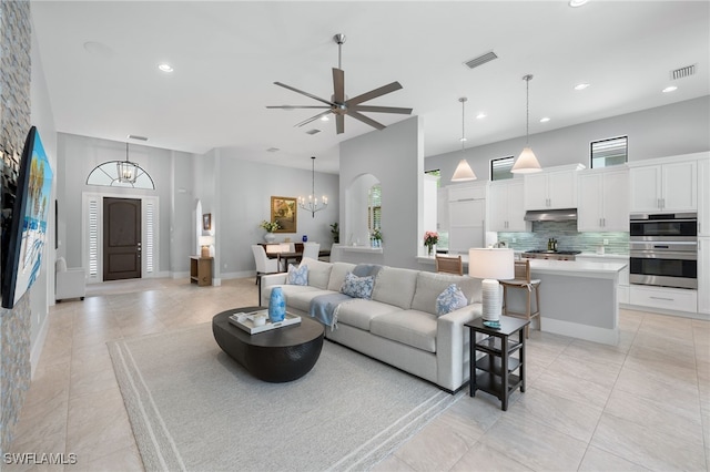 tiled living room featuring ceiling fan with notable chandelier and a high ceiling