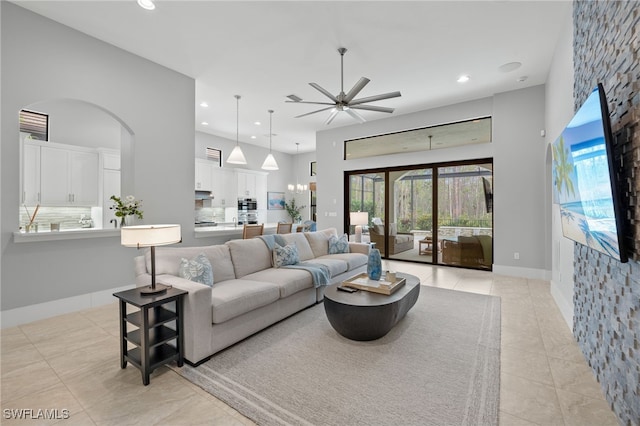 tiled living room with ceiling fan with notable chandelier and a high ceiling