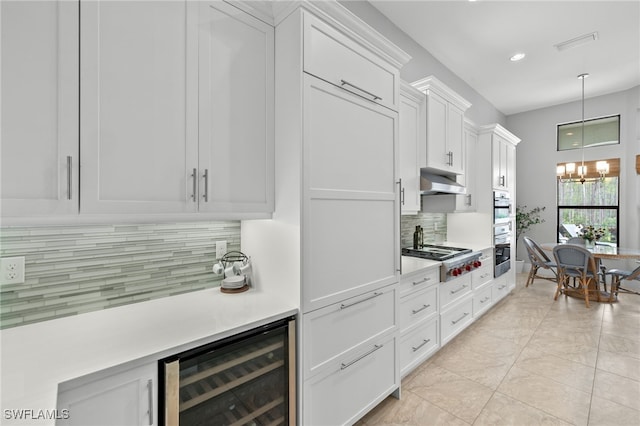 kitchen with a chandelier, pendant lighting, stainless steel gas stovetop, beverage cooler, and white cabinets