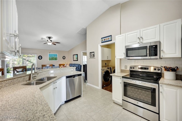 kitchen with vaulted ceiling, appliances with stainless steel finishes, sink, independent washer and dryer, and light stone countertops