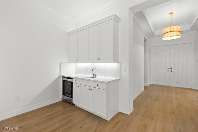 interior space featuring hanging light fixtures, white cabinetry, ornamental molding, light hardwood / wood-style floors, and beverage cooler