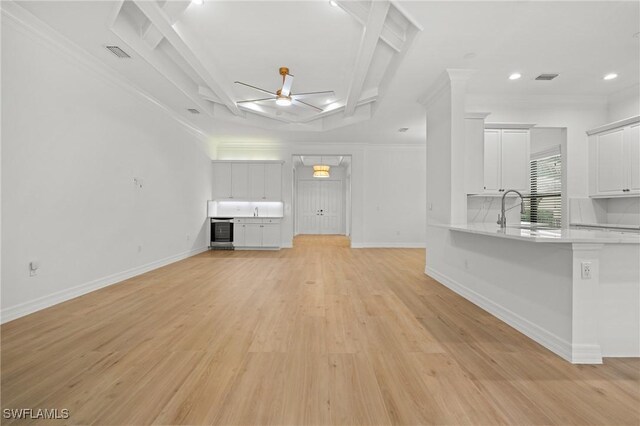 unfurnished living room featuring crown molding, light hardwood / wood-style flooring, ceiling fan, sink, and coffered ceiling